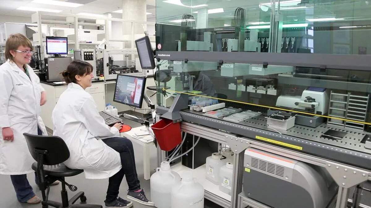 Two researchers wearing lab coats look at a computer. 