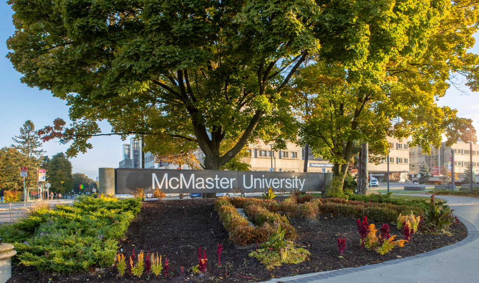 The McMaster University sign outdoors in front of a tree.